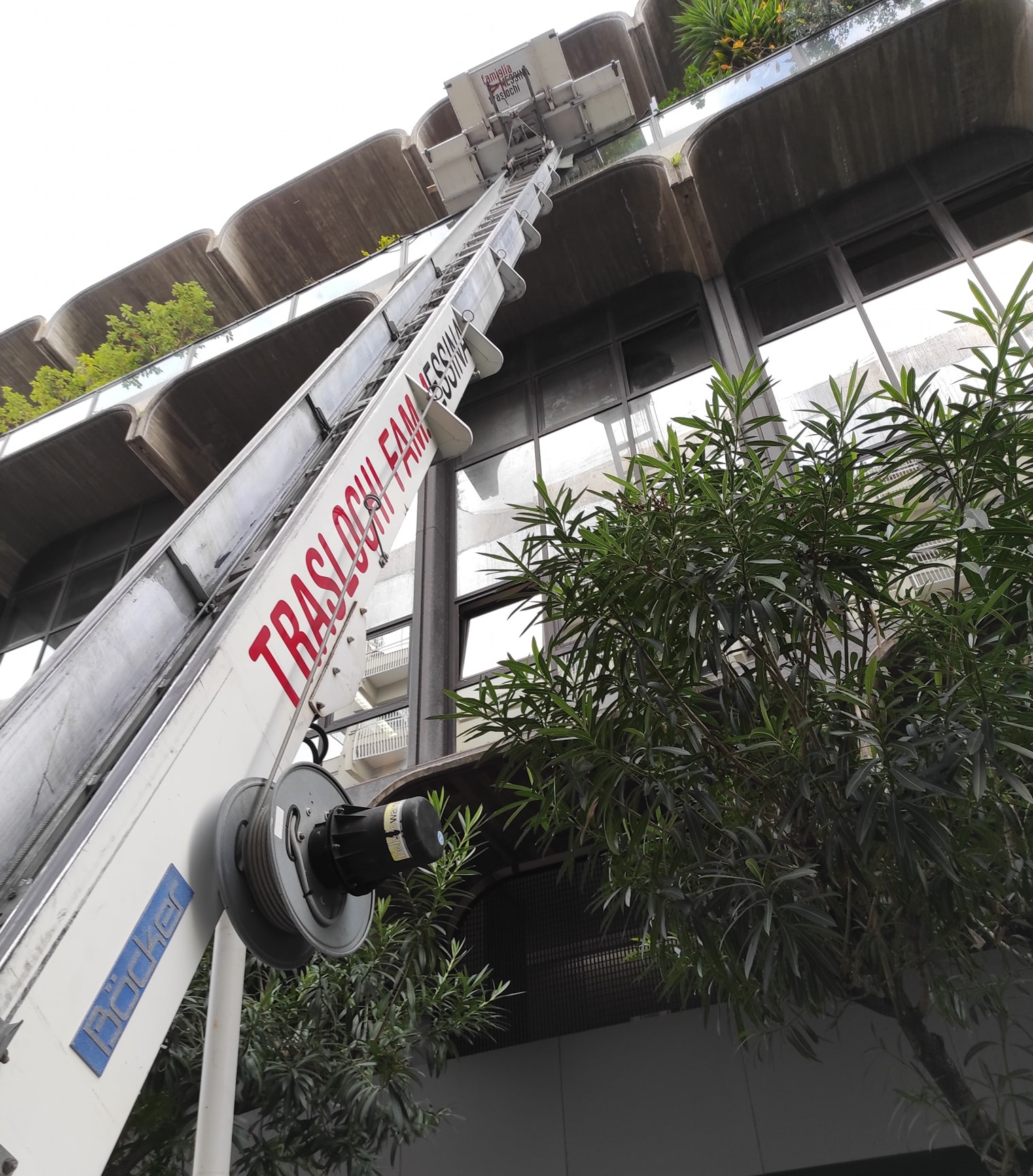 Scala elevatrice Böcker con scritta Traslochi Famiglia Messina appoggiata a un palazzo con balconi in cemento e oleandri