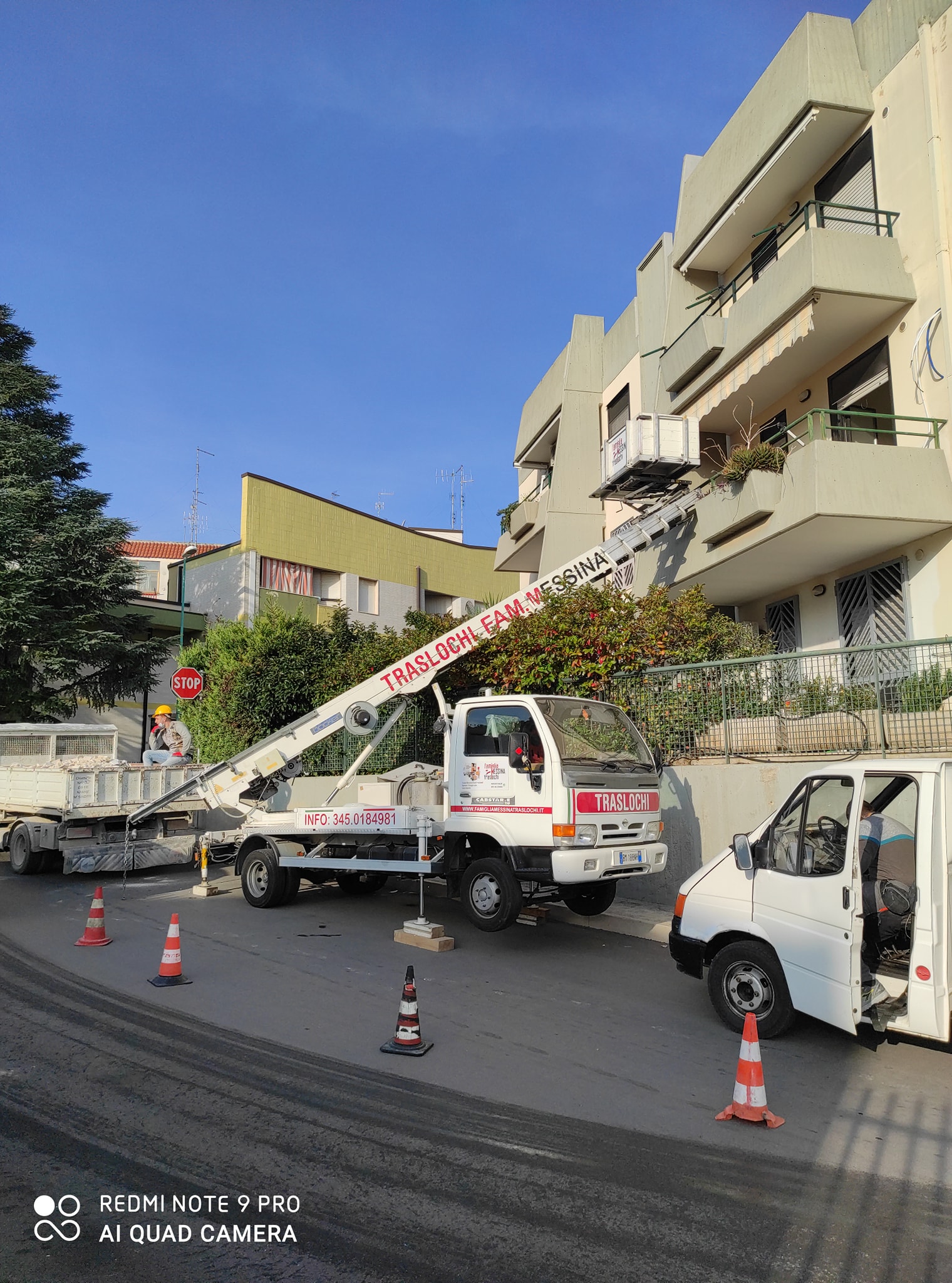Camion bianco con scala TRASLOCHI FAM. MESSINA e piattaforma al balcone di un palazzo color crema, tra coni stradali