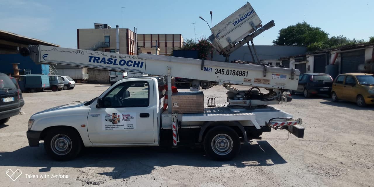 Pick-up bianco Famiglia Messina con autoscala TRASLOCHI e numero 345.0184981 in un piazzale sterrato